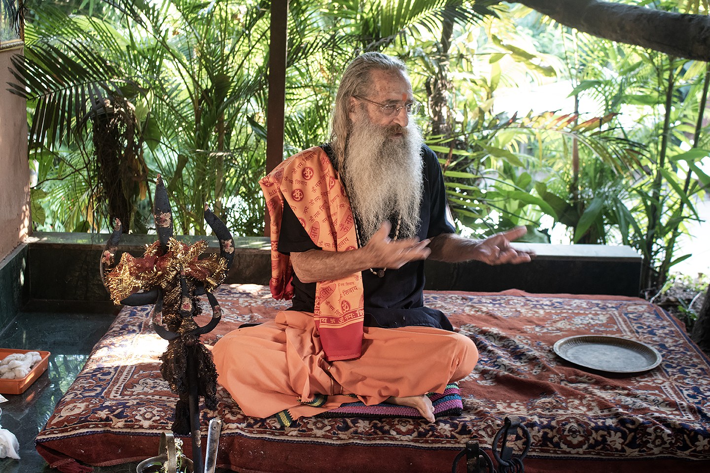 Baba Rampuri seated at his dhuni in Goa, speaking, with his trident beside him